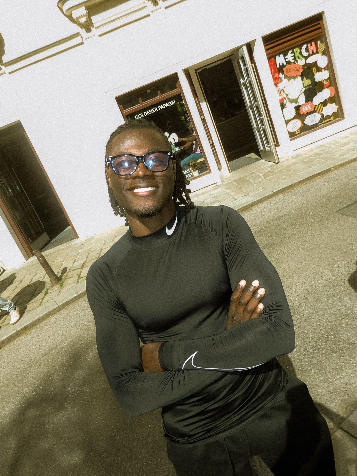Milianyen in a black Nike top, arms crossed, smiling on a Vienna street